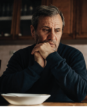 An older man looks off in front of an empty bowl.